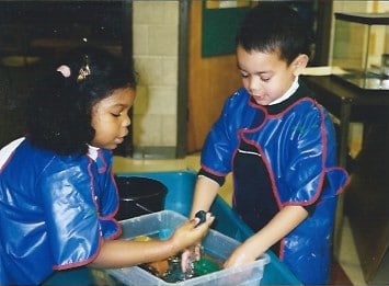 Two children play together with a tub of water