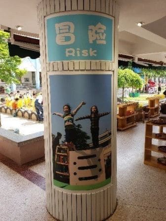A pillar of two children holding out their arms jumping off of an object with a poster with 'Risk' written on it