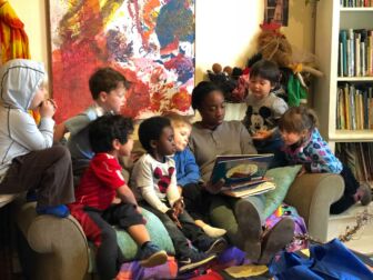 A group of children gather around Kisha Reid sitting on a couch with a book