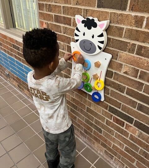 A child playing with an educational wall-mounted toy featuring shapes and colors.