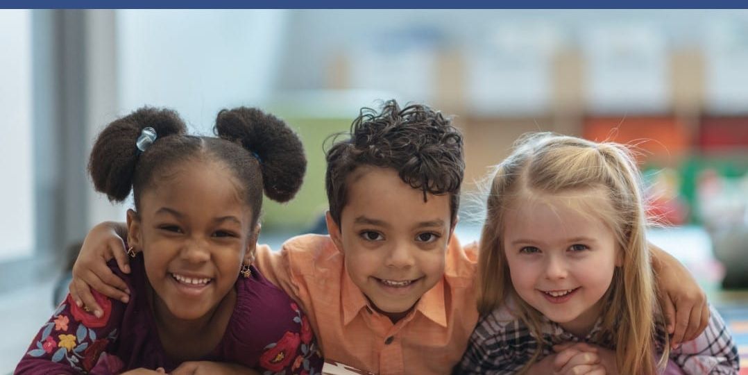 Three smiling children engaging in a classroom activity, representing the focus on early childhood education and care at the 6th annual summer institute.