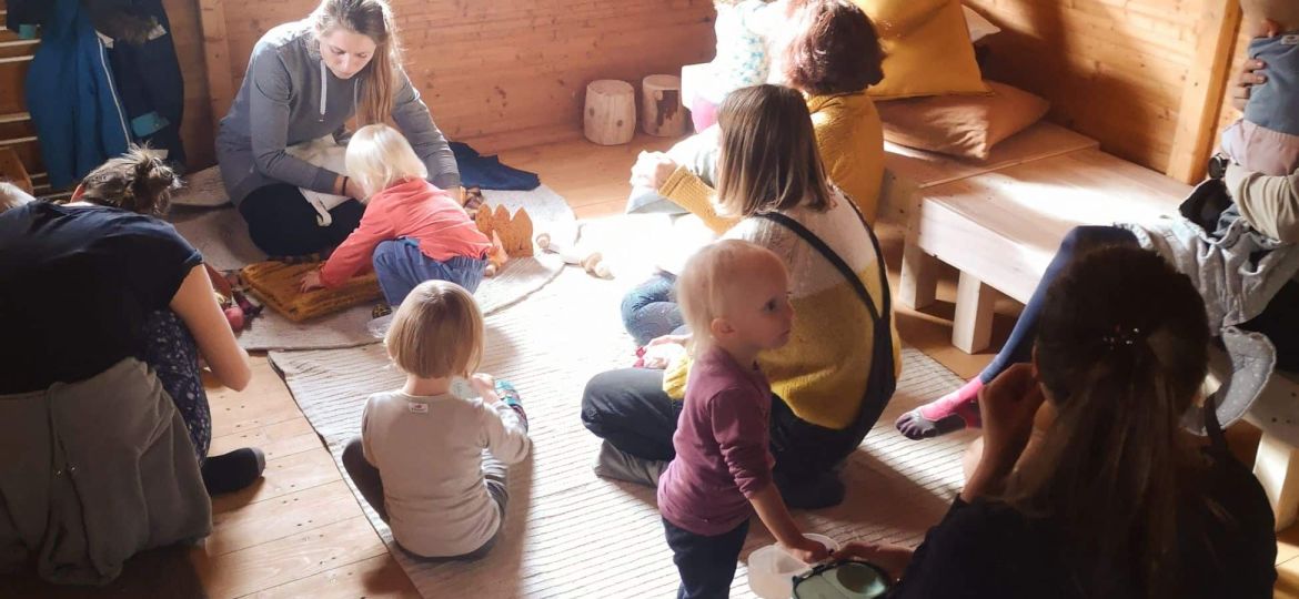 Group of people gathered indoors, sitting and interacting in a cozy wooden room.