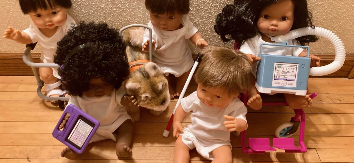 Five dolls dressed in white sit on a wooden floor, surrounded by various playtime medical equipment, including a toy stethoscope, blood pressure monitor, and a stuffed animal.