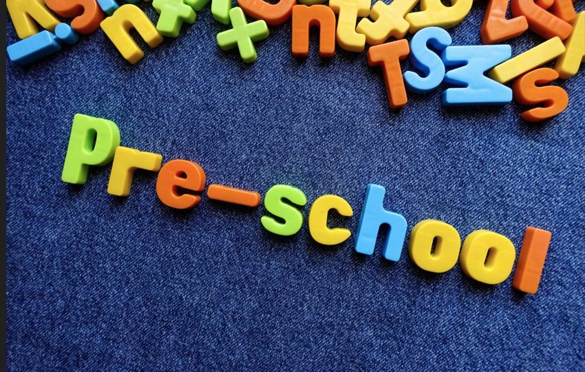 Colorful magnetic letters spell "pre-school" on a blue surface, with additional letters scattered above.