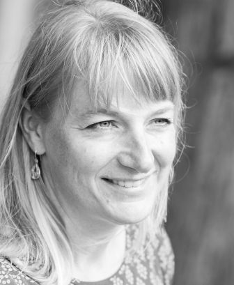 A woman with light-colored hair and earrings is smiling, looking slightly to the right. The image is in black and white. A woman with light-colored hair and earrings is smiling, looking slightly to the right. The image is in black and white.
