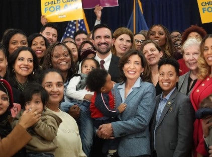 A diverse group of people, including adults and children, gather for a photo. Some hold 